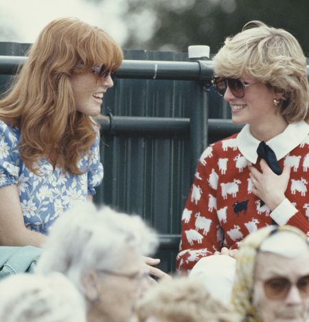 Sarah Ferguson sitting and talking to Princess Diana, who is wearing a red sheep sweater, smiling at a polo match