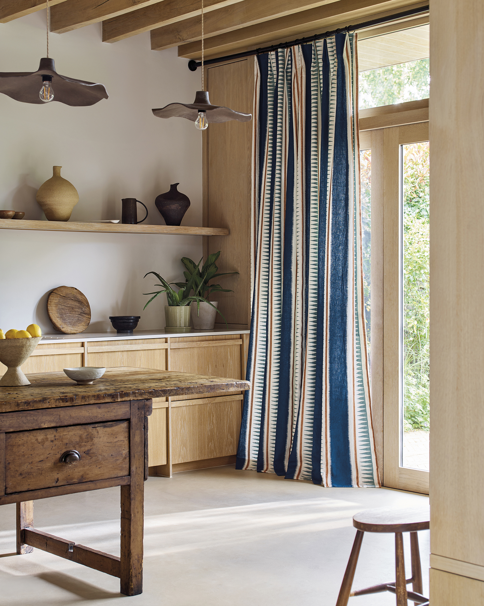 a kitchen with wooden cabinets and rustic island with blue striped curtains