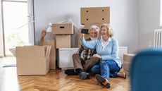 A senior couple sits on the floor with boxes, having moved.