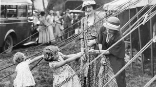 This charming snapshot, taken at the Abergeldie Castle Fete, behind the marquee in which the two little Princesses sold white heather in aid of the funds of Crathie Church, Scotland, June 9, 1933. Princess Elizabeth is enjoying a tug-of-war with a spring of heather, while Princess Margaret Rose busies herself with the guy ropes of the marquee. (Photo by PhotoQuest/Getty Images)