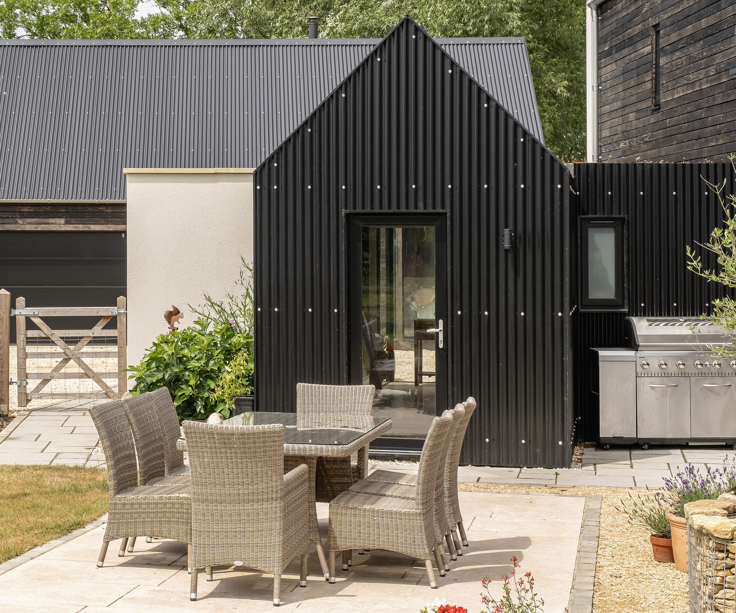 A stone patio in front of a black metal corrugated cladding over a self build home