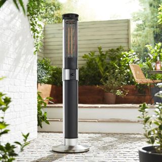 A black column patio heater standing on a patio surrounded by greenery