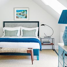 A white bedroom with a bed with a black bedframe and blue bedroom accessories