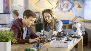 Girl and boy program cute robot with laptop