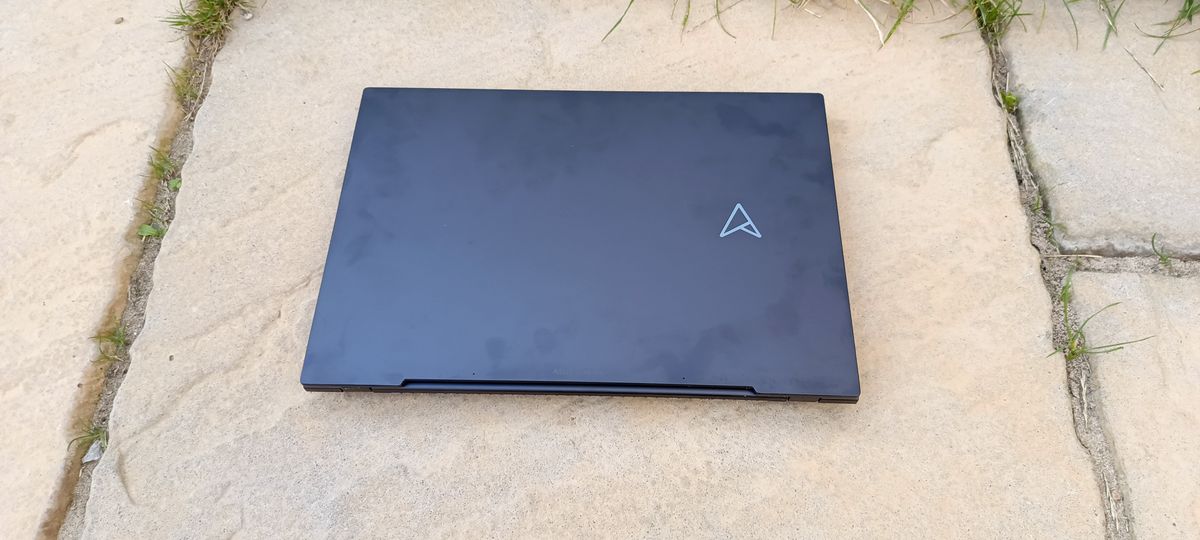 A black ASUS Zenbook Pro 14 OLED sitting on a patio in front of a grassy lawn