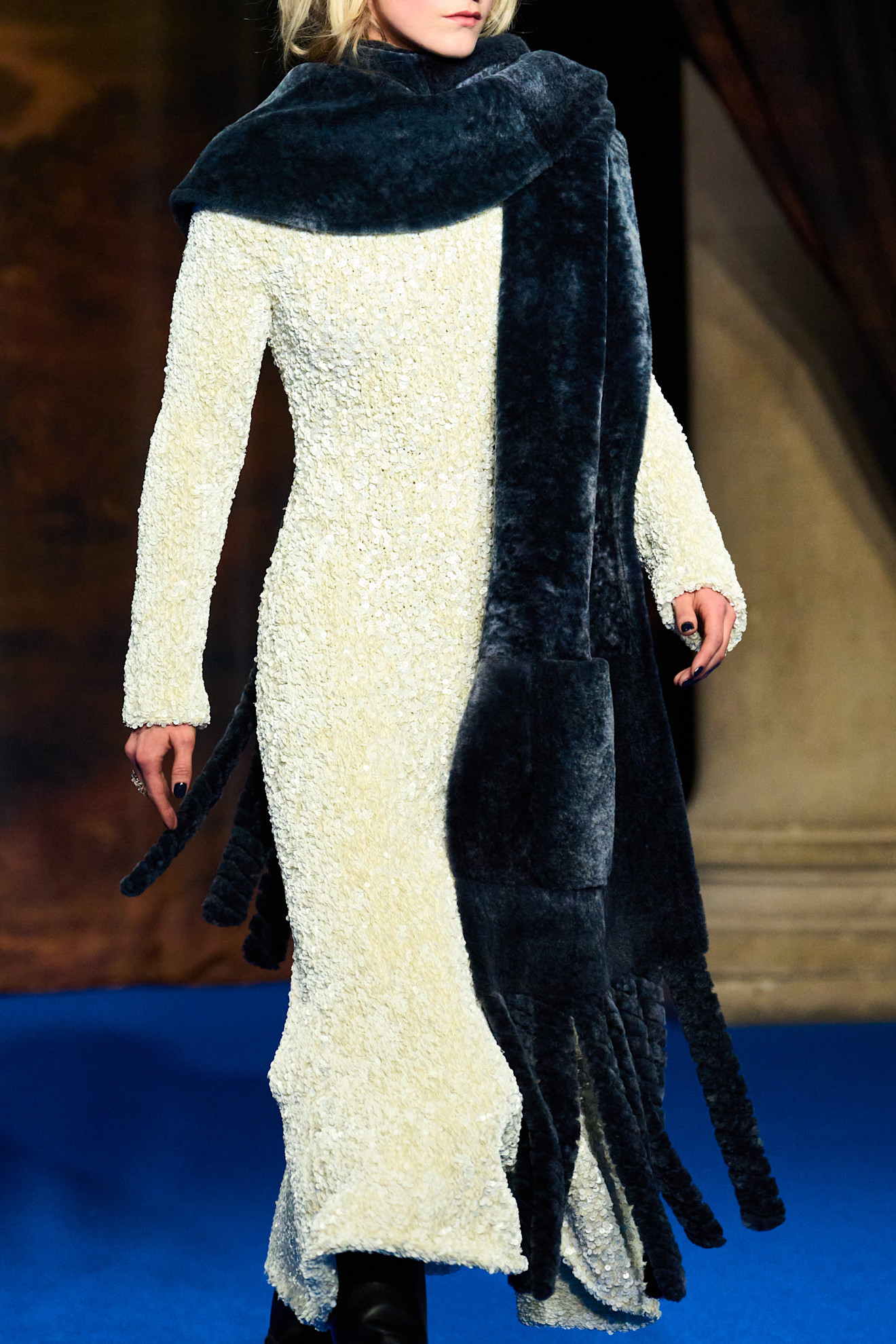 The fur accessory trend shown in Burberry's fall-winter 2025 collection in a close photo of a model wearing a white shearling dress with black boots and a navy blue long faux fur scarf