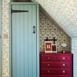 Wardrobe and chest of drawers in bedroom underneath wallpapered eaves