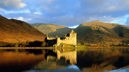 A photo of one of the castles in Scotland set against a Loch with mountains behind 