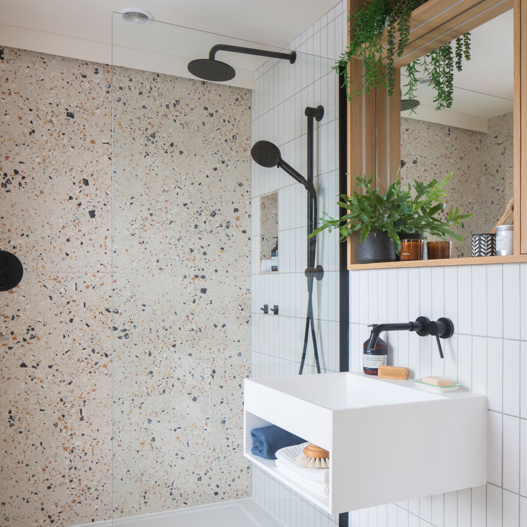 White tiled bathroom with terrazzo tiled shower cubicle with black hardware