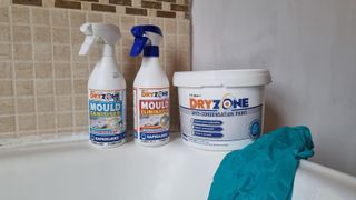 Mould sanitiser and eliminator spray bottles with anti condensation paint and protective gloves on the edge of a bath