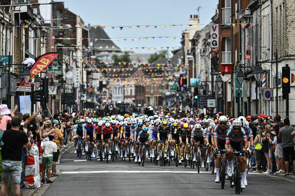 The pack of riders (peloton) cycles through the town of Carvin during the 1st stage of the 112th edition of the Tour de France cycling race, 184.9 km starting and finishing in Lille Metropole, northern France, on July 5, 2025. (Photo by Marco BERTORELLO / AFP)