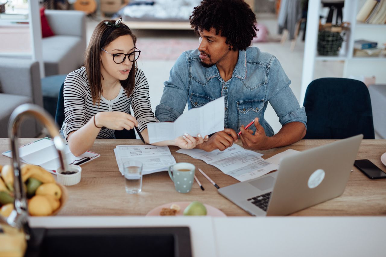 Two young adults discuss their budget at the kitchen counter.