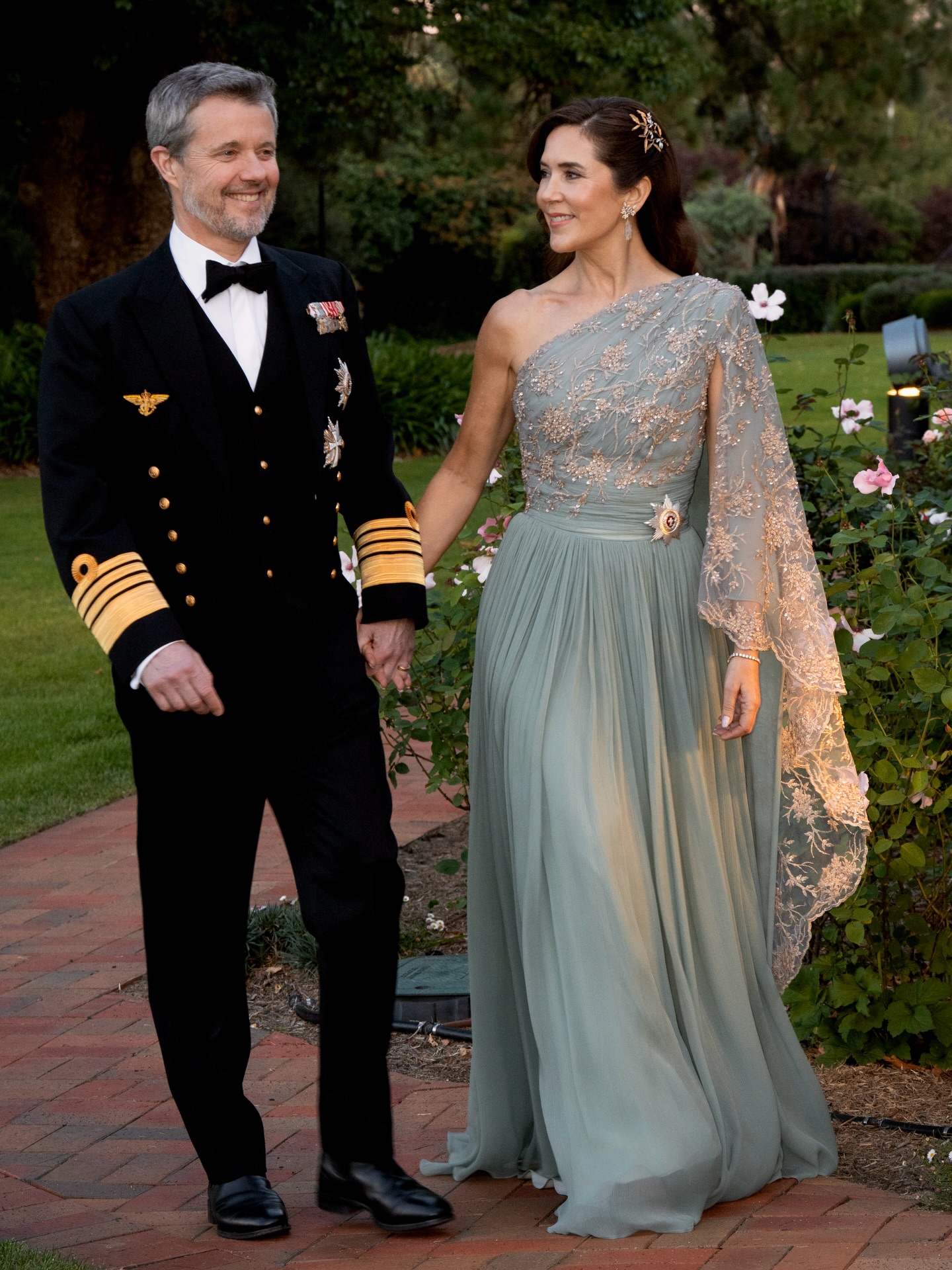 King Frederik in a military uniform holding hands with Queen Mary, wearing a mint gown