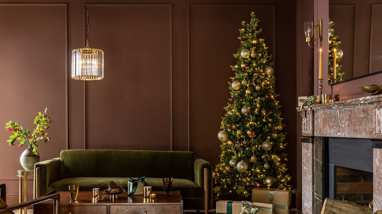 A slim Christmas tree in a burgundy living room beside a green velvet sofa