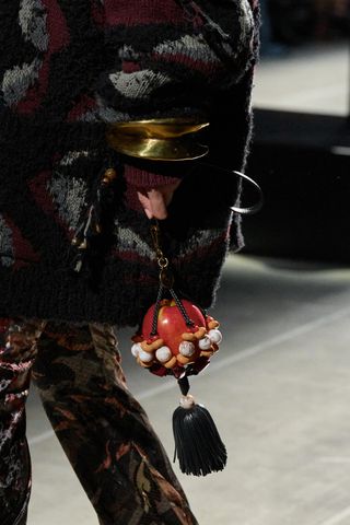A model in Etro Fall/Winter 2024 carries a maximal accessory of a macrame apple holder
