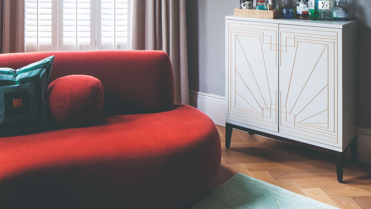 A living room with an art deco-style bar and a dark red-coloured curved sofa