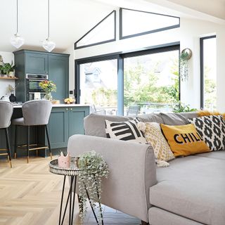 open plan blue kitchen with grey corner sofa and wooden herringbone flooring