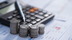 four stacks of coins next to a calculator and pen, all on top of financial papers