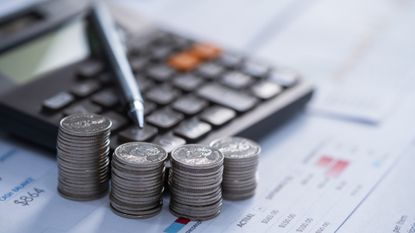 four stacks of coins next to a calculator and pen, all on top of financial papers