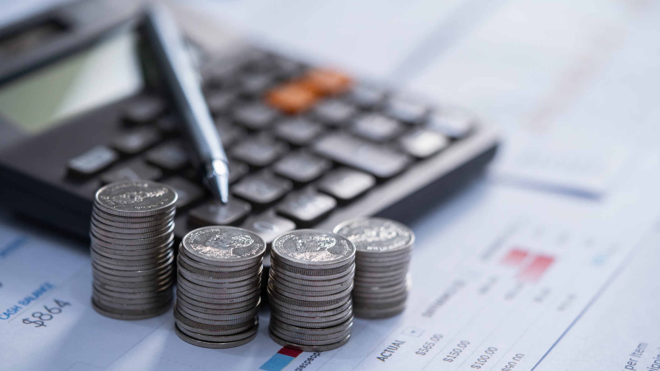 four stacks of coins next to a calculator and pen, all on top of financial papers