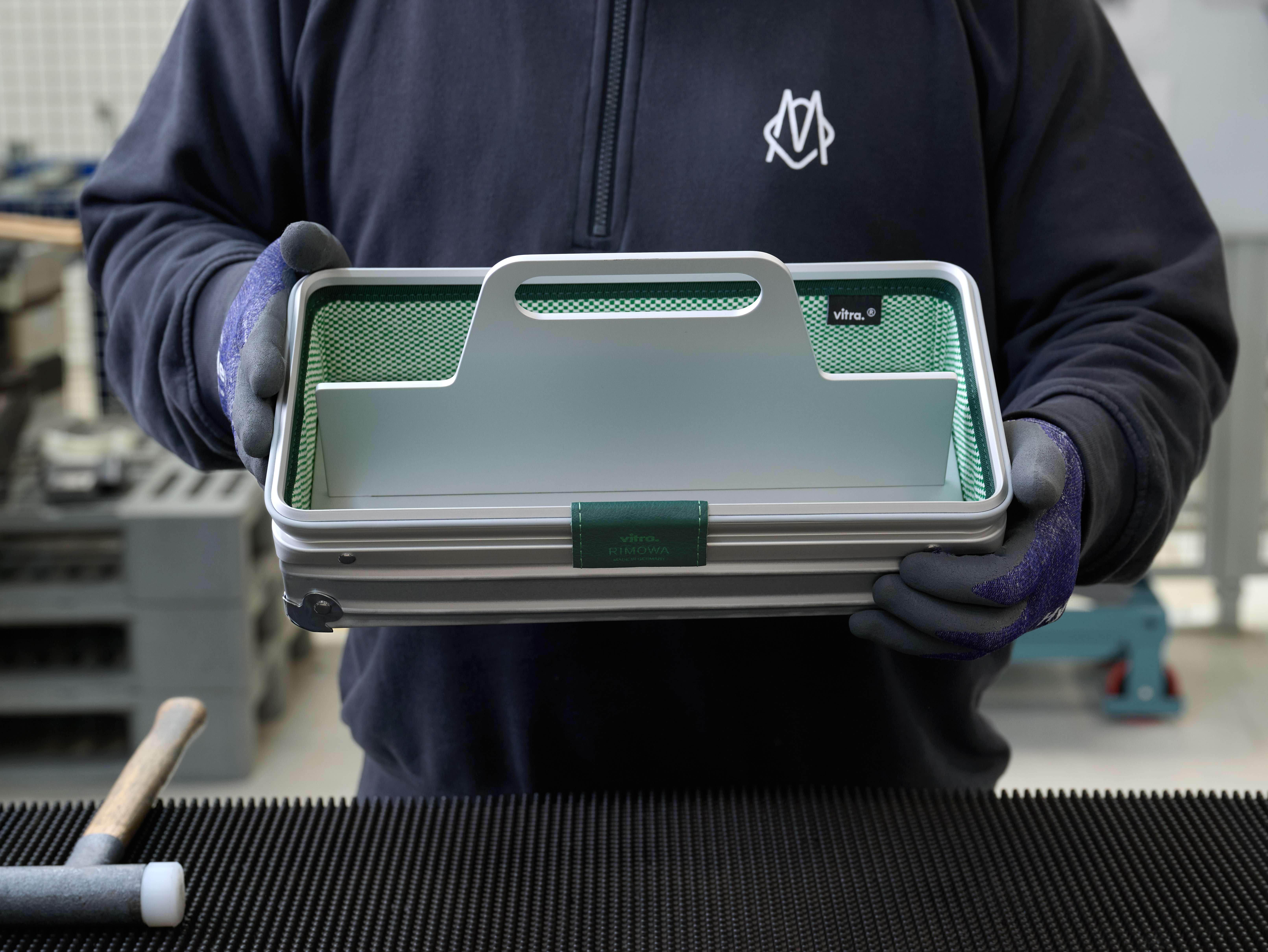 Person wearing gloves holding aluminium storage tray in production factory