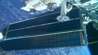 a view of two solar array panels, one overlapping the other, extending from a space station while in orbit over a blue planet
