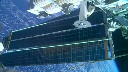 a view of two solar array panels, one overlapping the other, extending from a space station while in orbit over a blue planet