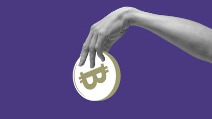 A hand holds a bitcoin against a purple background.