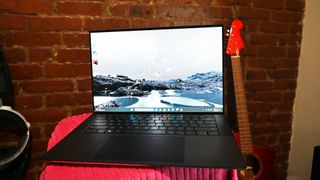 Memorial Day laptop deals Dell XPS 15 laptop on a red blanket next to a guitar with brick wall backgrounf