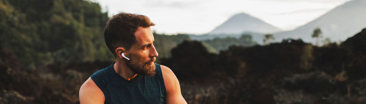A close-up picture of a man listening to his earbuds outdoors