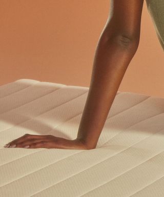 A woman pressing her hand against the Earthfoam Organic Mattress against a peach background.