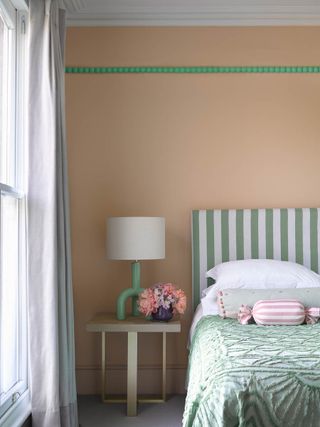 A peach bedroom with green details, a mstriped headboard and styled bedside table