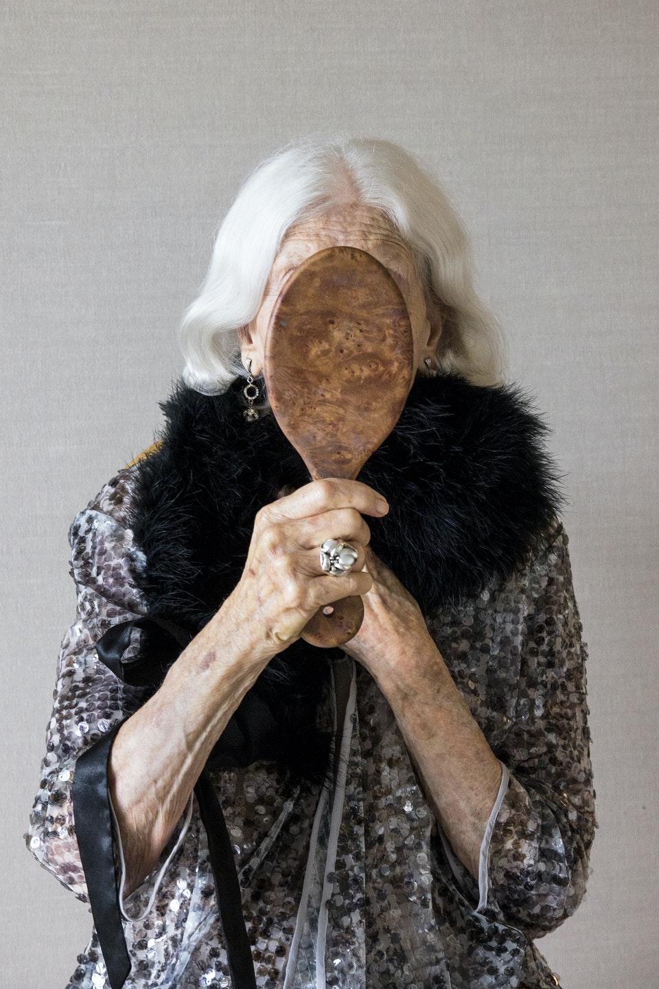 An older woman holding a mirror in front of her face