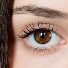 a close up of one hazel eye and eyebrow, with a small section of brunette hair over the face