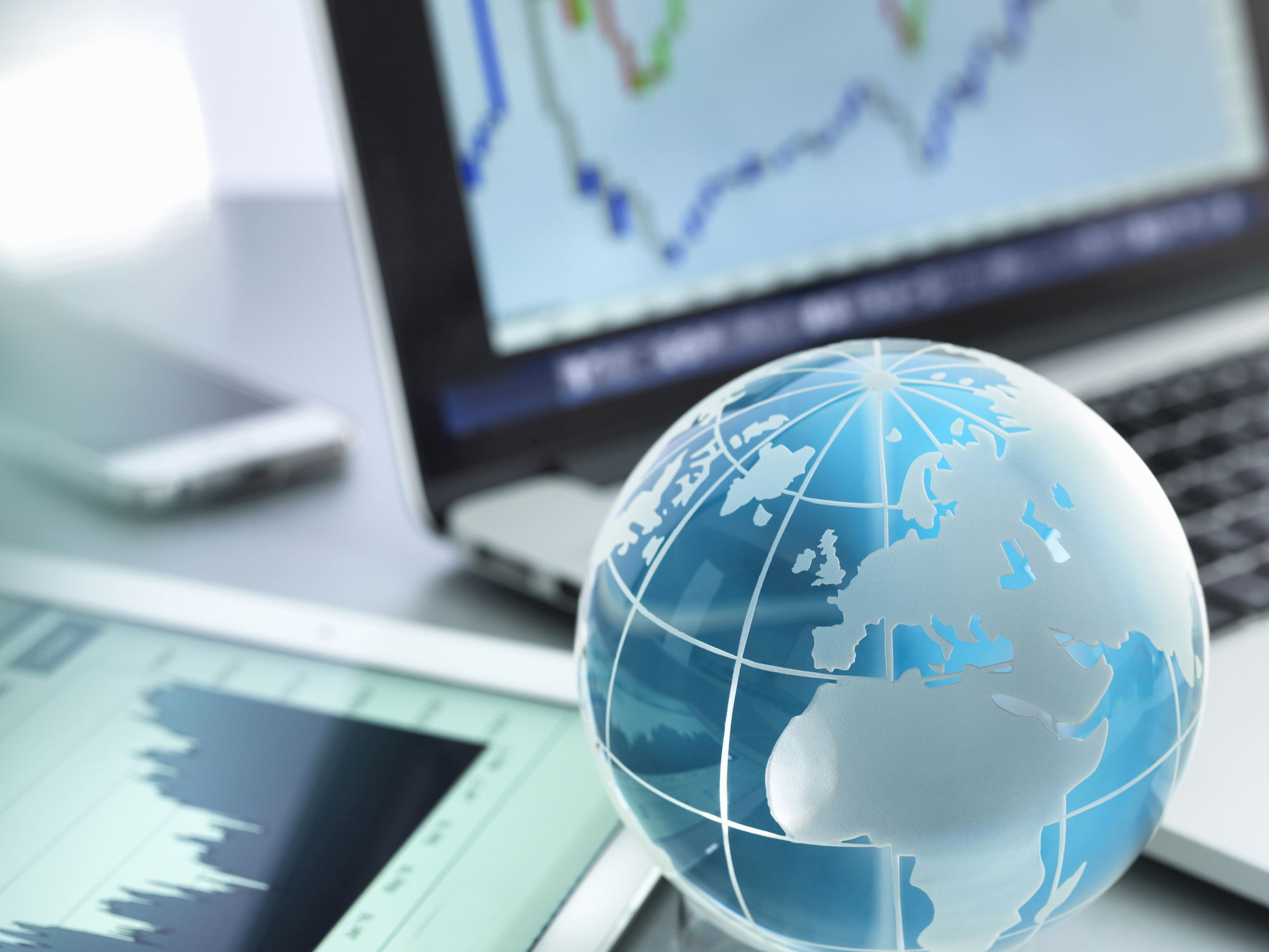 small globe spotlighting Europe placed next to a laptop and tablet with stock charts
