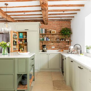 kitchen with exposed brick walls and two toned green cabinetry sandstone flooring