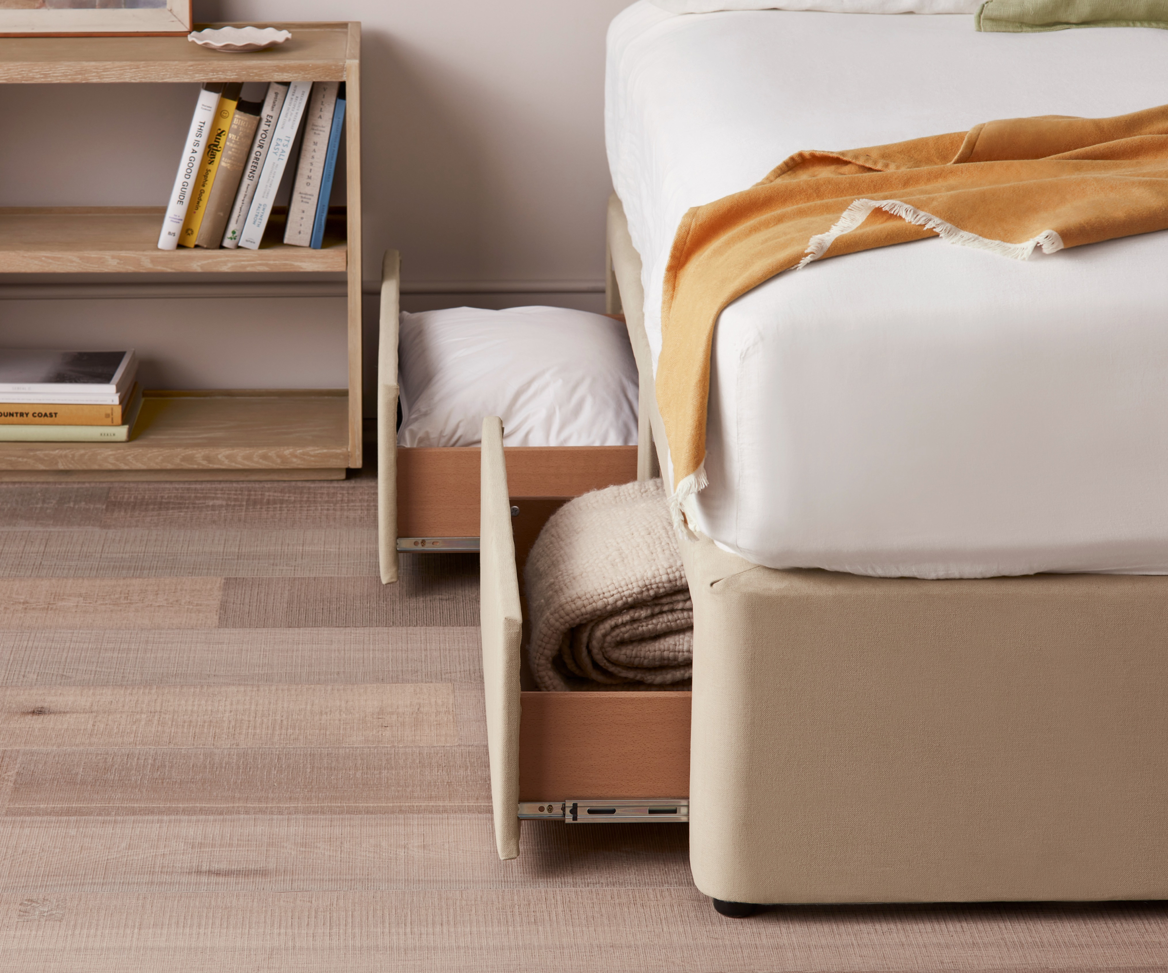 low divan bed with drawers below opened showing bedding and low wooden shelf unit to the one side