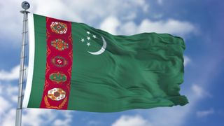 The Turkmenistan flag flying against a blue sky with light, fluffy clouds