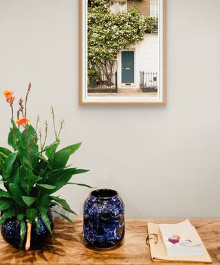 A beige wall with a nature print and a table with a pltant, blue vase, and paper