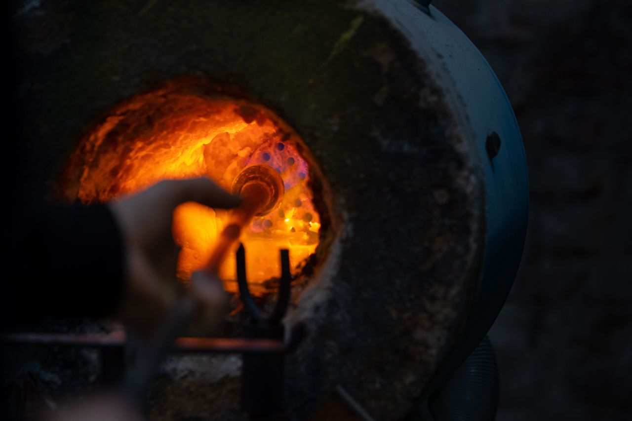 The detail of a glassmaking furnace shows a man at work in front of one of its ovens introducing a piece of glass into it.