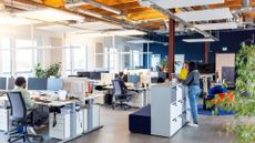 Open plan office space with staff working at desktop computers and others mingling around.