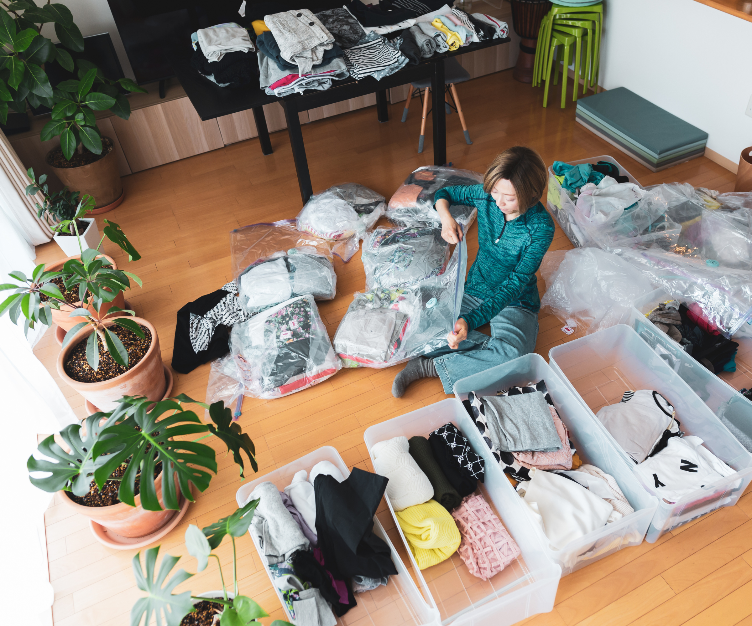 Woman organising boxes of clothes on the floor of a room with plants