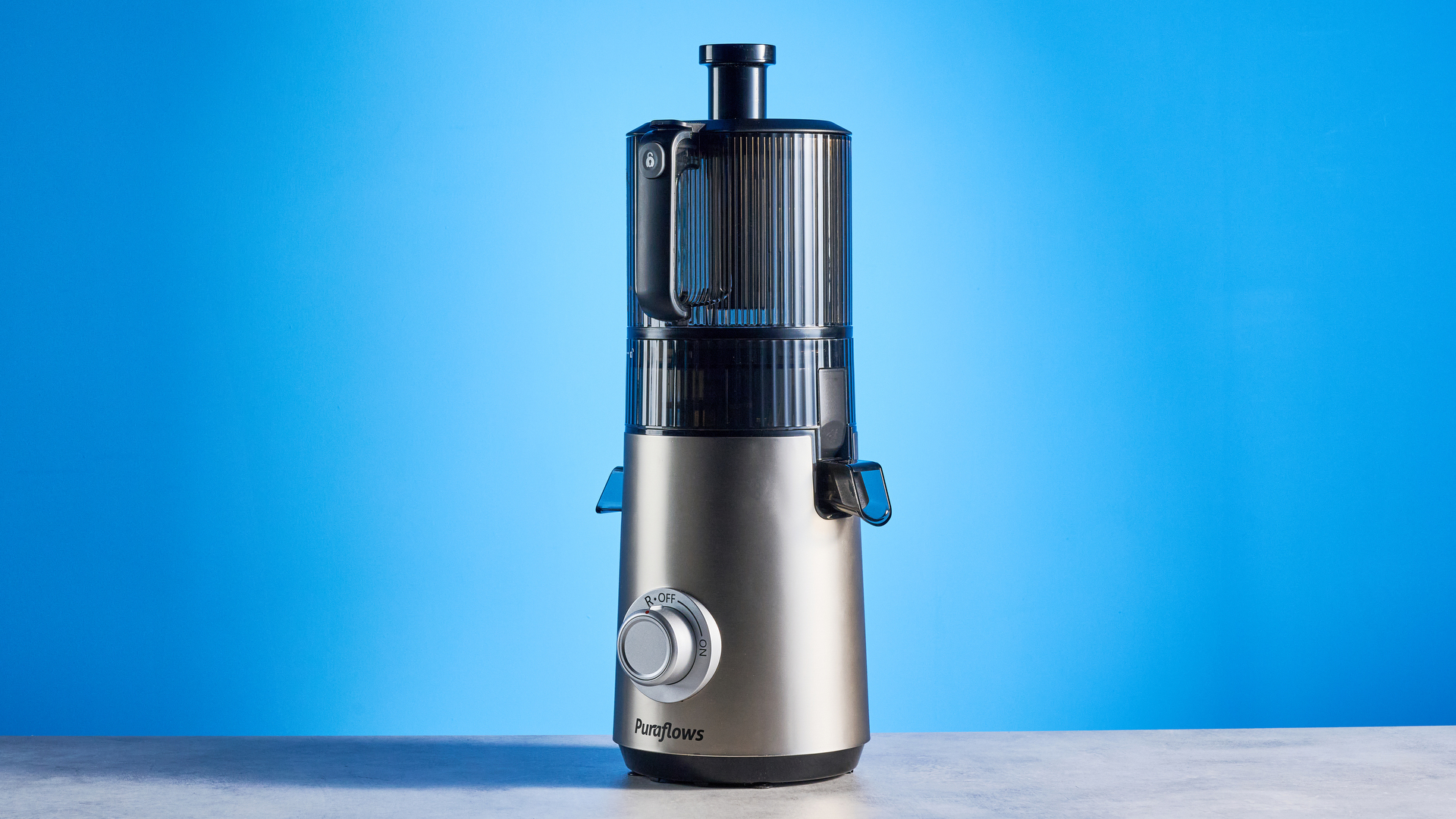 Puraflows Auramist Cold Press Juicer and accessories photographed in front of a blue background