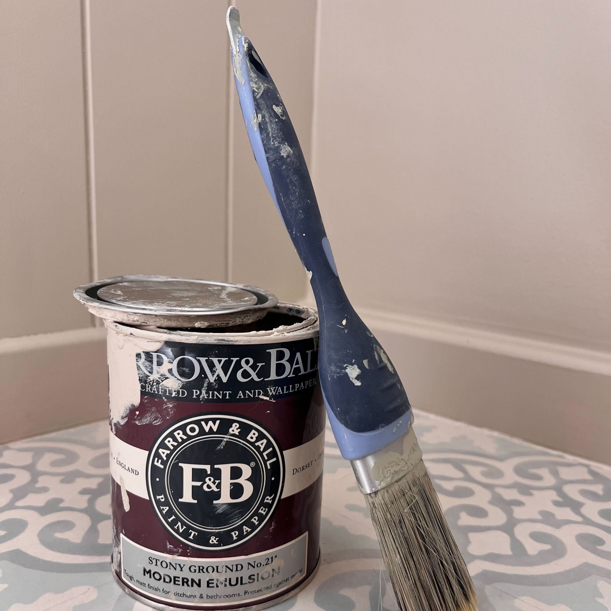 The Dulux Perfect Finish paint brush with a tin of Farrow & Ball paint, on a blue and white patterned, tiled floor.