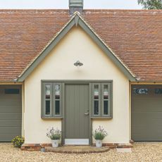 A soft yellow-painted house with a sage green front door and matching windows and garage doors