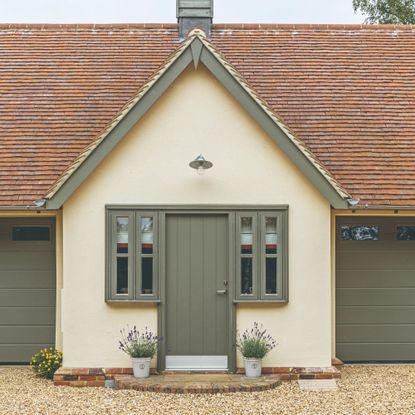 A soft yellow-painted house with a sage green front door and matching windows and garage doors