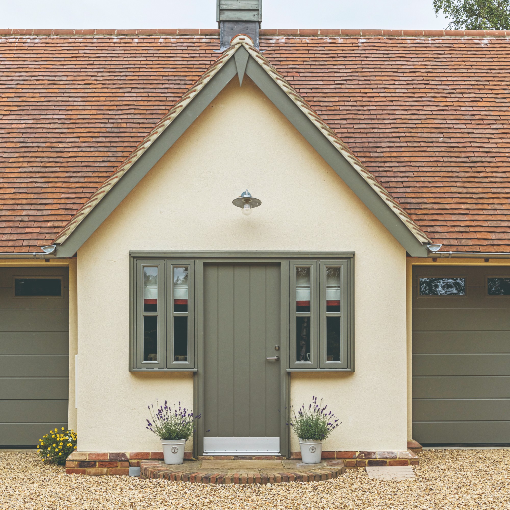 A soft yellow-painted house with a sage green front door and matching windows and garage doors