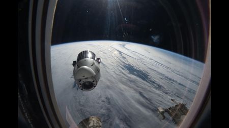 A view out of the window of the ISS sees the SpaceX Dragon capsule with Earth in the background. 