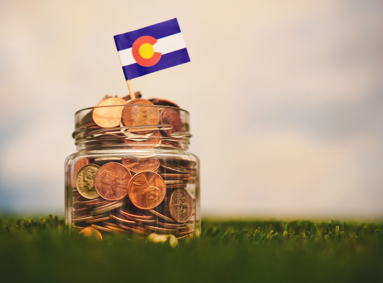 jar of coins with a miniature Colorado flag on top sitting on grass.