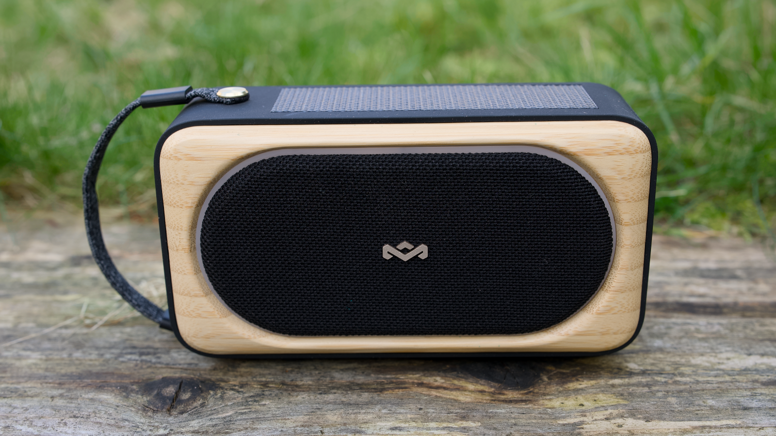 House of Marley Roots Solar Bluetooth speaker outdoors in a garden, on a wooden bench.
